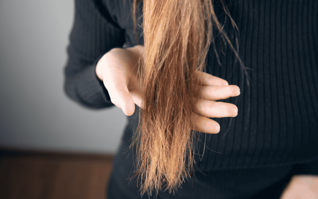 A person wearing a black sweater holds the dry, frizzy ends of their long, light brown hair.