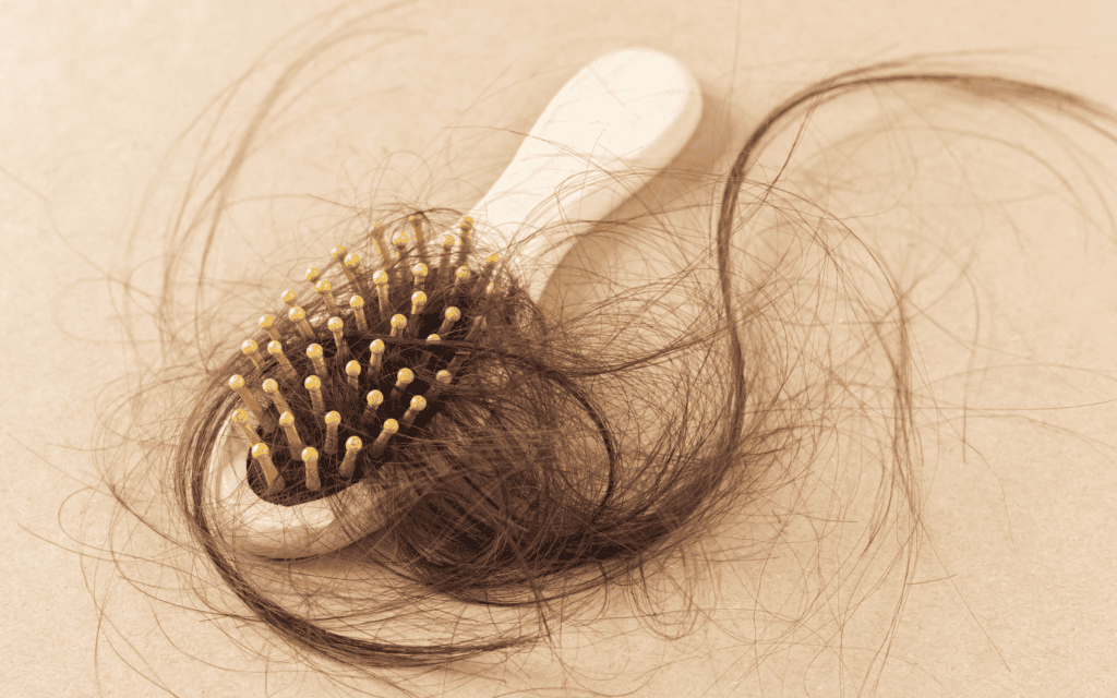 A hairbrush with many brown hairs tangled in its bristles, lying on a light surface.